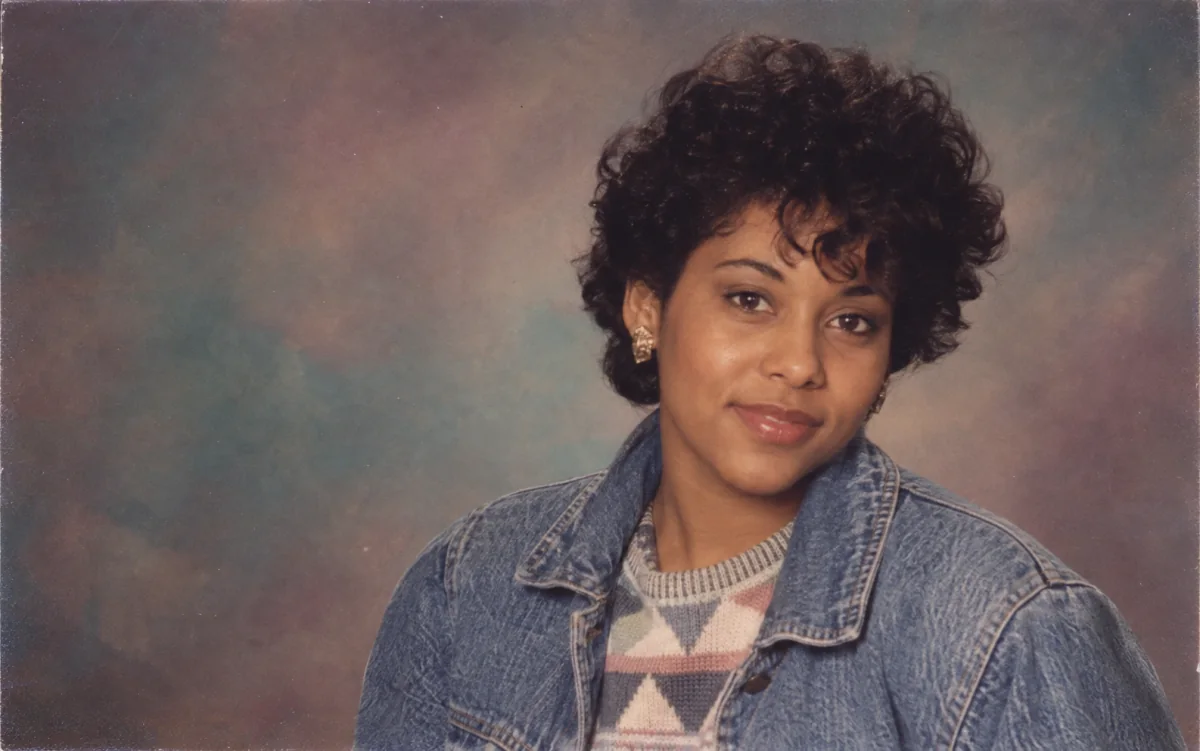 AI-generated example of an adult in a 1985 department-store portrait with curly hair, denim, and an analog painted backdrop