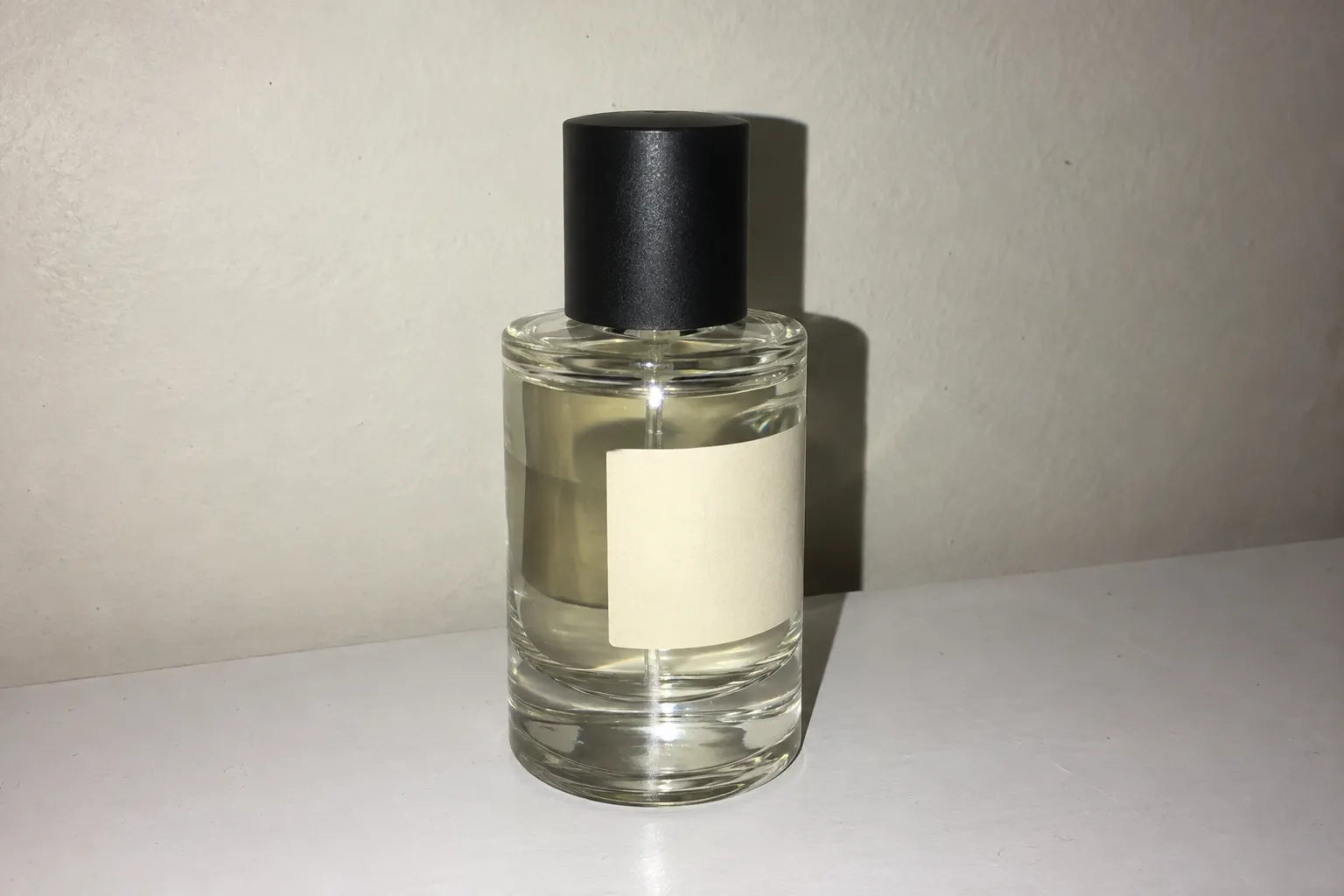 Glass perfume bottle on a white table shot with harsh on-camera flash and a hard shadow behind it.