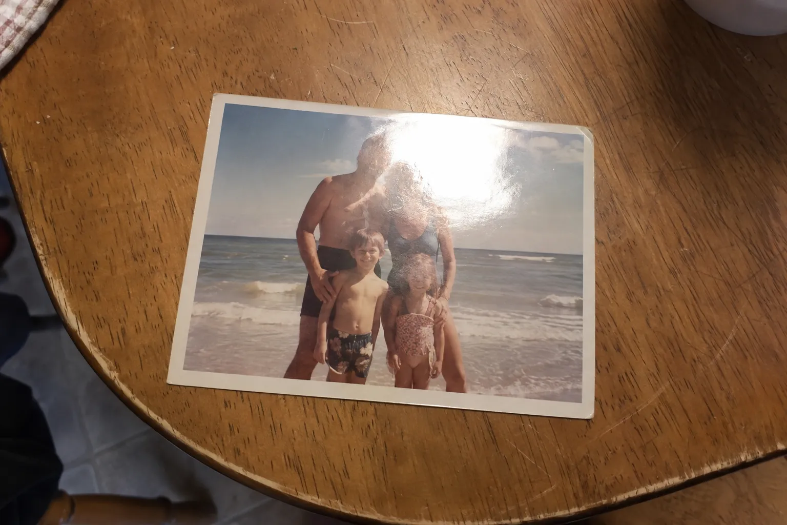 Phone photo of a vintage family beach print on a table with a bright lamp glare patch on the glossy paper.